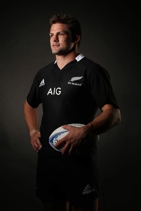 a man holding a rugby ball in his right hand and wearing a black jersey with white letters on it