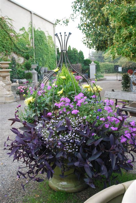 purple and yellow flowers are in a green vase on the ground near a park ...