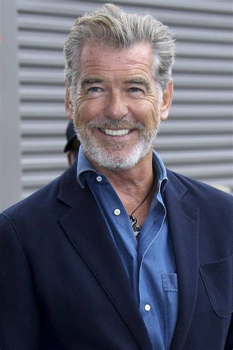 an older man in a blue shirt and blazer smiles at the camera with his hands in his pockets