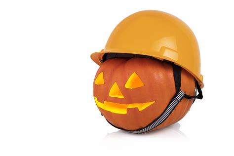 Orange pumpkin with glowing eyes in a yellow construction helmet, hard hat. Halloween concept ...