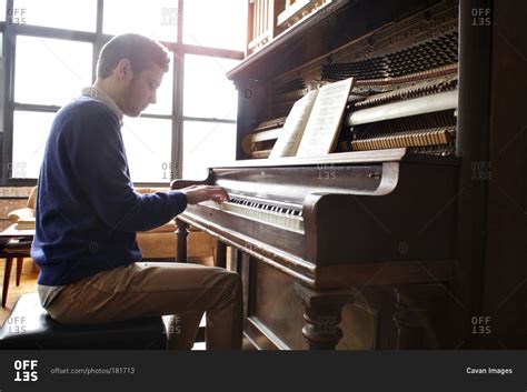 Young man playing an upright piano stock photo - OFFSET