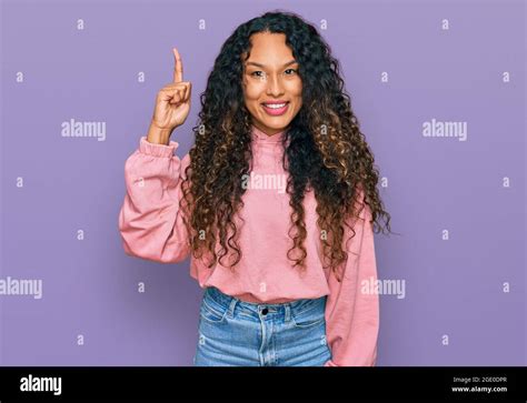 Young hispanic woman with curly hair wearing casual sweatshirt pointing finger up with ...