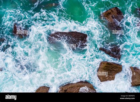 Top aerial view of blue waves crashing on rocky Australian coastline. Summer seascape with birds ...