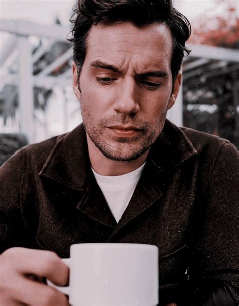 a man holding a white coffee cup in his hand and looking down at the ground