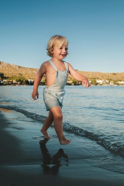 Premium Photo | Barefoot positive little boy walking on sandy beach of wavy sea