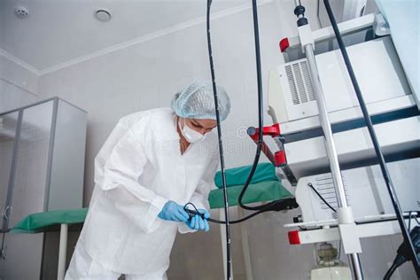 A Young Female Endoscopist in a White Protective Suit, Cap and Gloves Prepares the Equipment for ...