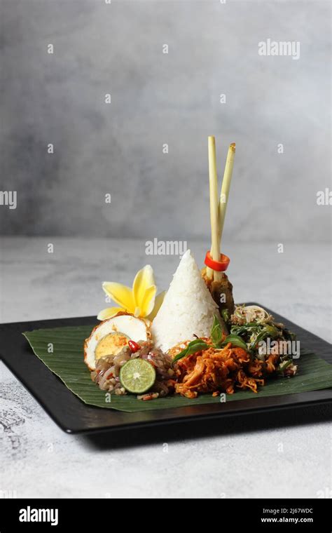 Tasty spicy nasi bali with chili egg, chicken satay and salad veggie on black plate white ...