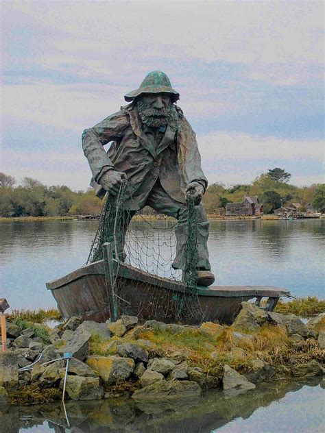 a statue of a man standing on top of a boat next to a body of water