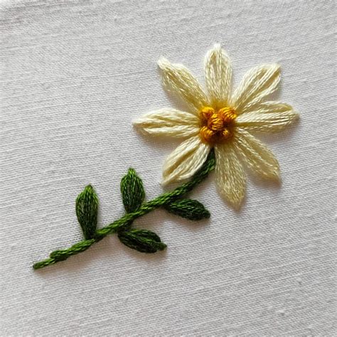 a close up of a flower on a piece of white fabric with green leaves and ...