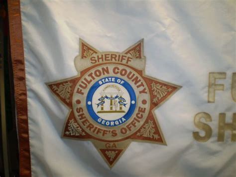 the sheriff badge is displayed on a white flag that says fulton county sheriffs office