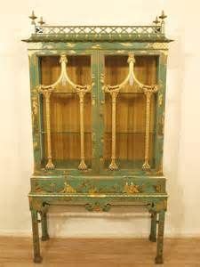 an antique green and gold china cabinet with glass doors on the front, sitting on a hard wood floor