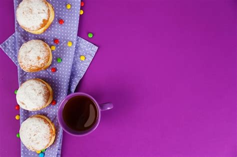 Premium Photo | Delicious donuts with powdered sugar and cup of tea on purple surface top view