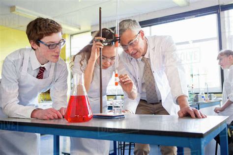 Chemistry teacher guiding high school students conducting scientific ...