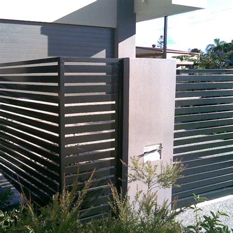 a black and white fence next to a building with plants in front of it ...