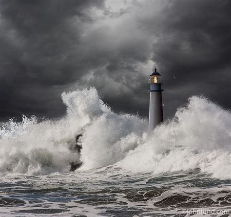 A keeper stands watch atop this lighthouse in a raging ocean storm with dark clouds and crashing ...