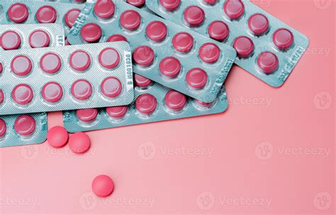 Pink round tablets in blister pack and some on pink background. Pharmaceutical industry. Top ...