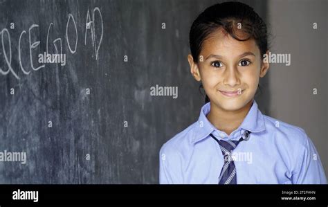Happy Indian school girl child standing in front of black chalkboard background. Education ...