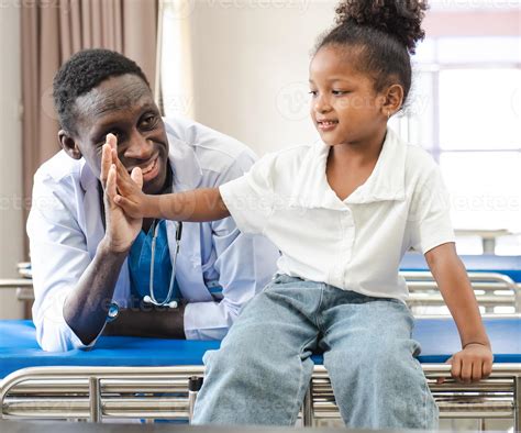 Child patient sitting on hospital bed with African doctor for medical ...