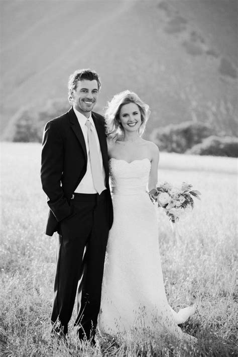 a bride and groom pose for a photo in a field with mountains in the background