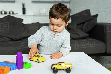 Selective focus of little kid playing with toy cars at table in living ...