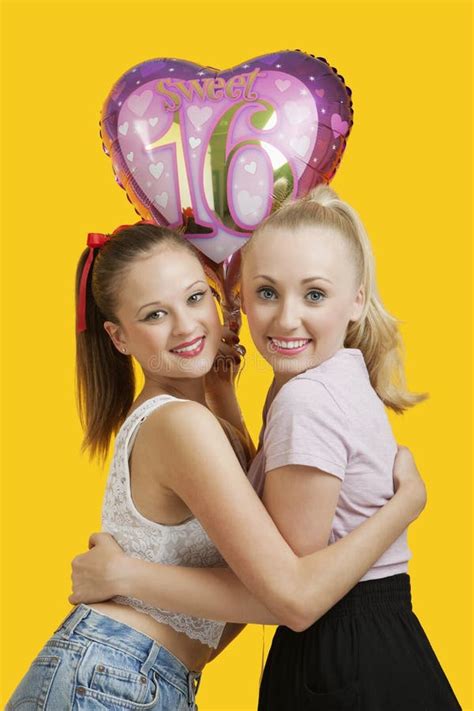 Portrait Of Two Happy Young Women With Birthday Balloon Hugging Over Yellow Background Stock ...