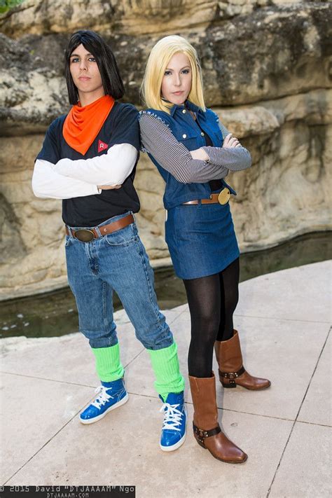 two people standing next to each other in front of a rock wall and water feature