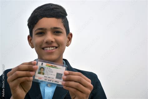 Indian school boy wearing dark blue school uniform, with smiling face shows her blurred aadhar ...