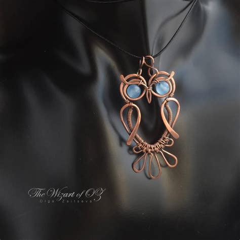 an owl pendant with blue eyes on a black mannequin neckline, hanging from a leather cord