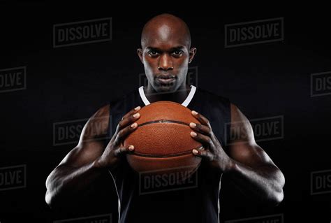 Portrait of afro american male basketball player with a ball over black background. Fit young ...