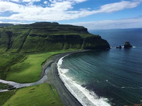 an aerial view of the ocean with cliffs in the distance and green grass on both sides