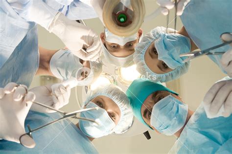 Below view of surgeons holding medical instruments in hands and looking ...