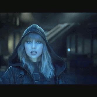 a woman with blonde hair wearing a black hoodie and looking at the camera in a dark room