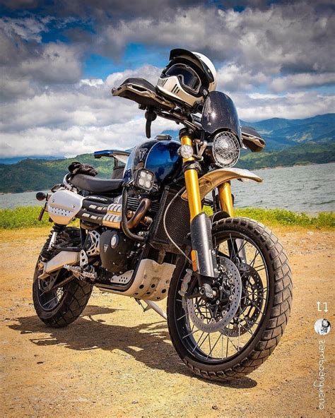 a motorcycle parked on the side of a dirt road next to a body of water