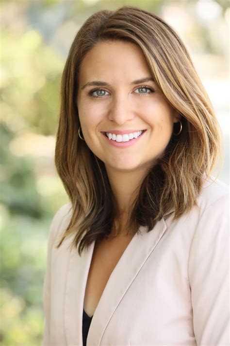 a woman with long hair smiling at the camera and wearing a white blazer ...