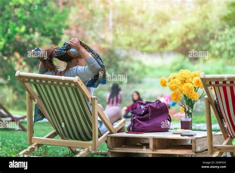 Back view of Asian senior woman sitting on garden chair and by the table in garden. Summer ...