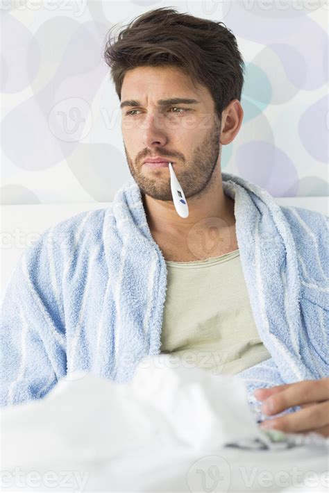 Sick man with thermometer in mouth sitting on bed 960942 Stock Photo at Vecteezy