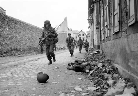 Soldiers of the 3rd U.S. Army storm into Coblenz, Germany, as a dead comrade lies against the ...