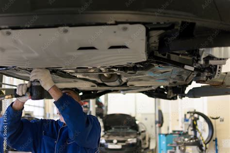 The car is lifted on a lift in a car service for repair. A professional mechanic is repairing a ...