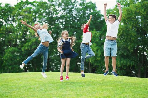 Adorable happy multiethnic kids playing and jumping on green meadow in park Stock Photo by ...