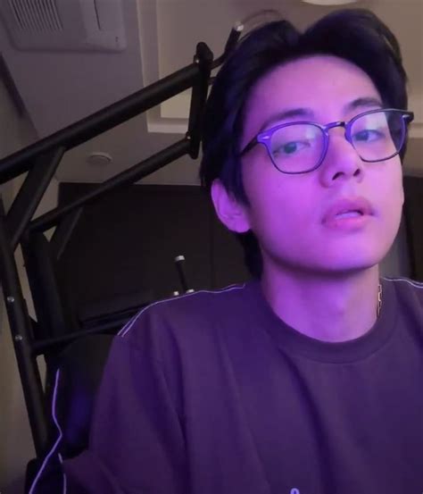 a young man wearing glasses sitting in front of a computer monitor with headphones on