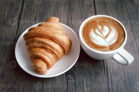 Freshly baked delicious croissant and cup of beautiful morning coffee on wooden breakfast table ...