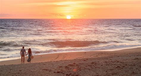 two people walking on the beach at sunset