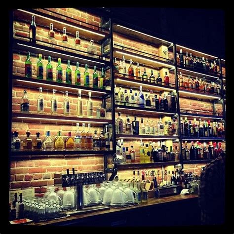 the shelves are full of liquor bottles and glasses on display in front of a brick wall