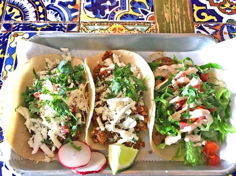 three tacos with meat, lettuce and radishes on a tray