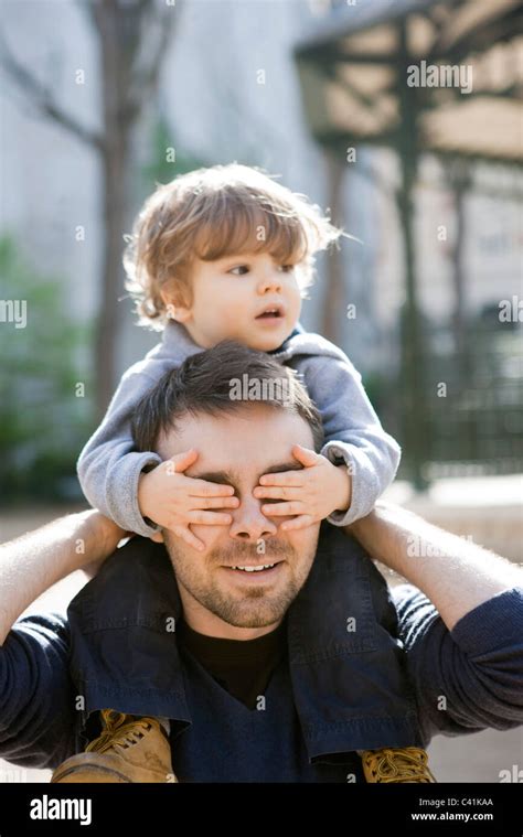 Father carrying toddler son on his shoulders, son covering father's eyes with his hands Stock ...