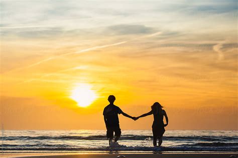 Silhouettes Of Man And Woman Holding Hands On The Beach At Sunset | Stocksy United