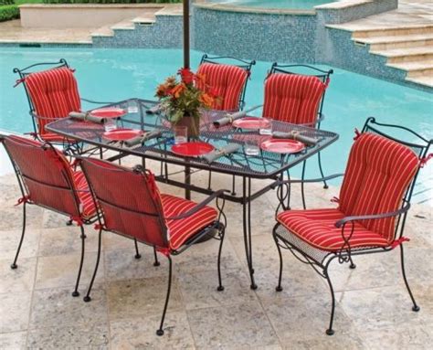 an outdoor dining table with red chairs and an umbrella over it next to a swimming pool