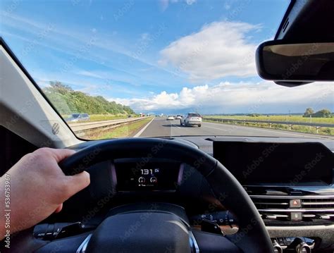 Driver point of view from car interior while driving a car on highway. Drivers hand holding ...