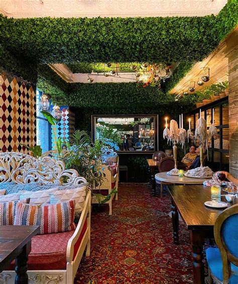 a restaurant with tables and chairs covered in plants on the walls, sitting next to each other