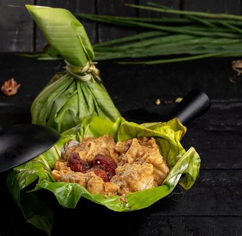 some food is sitting in a leafy wrapper on a black table with green leaves